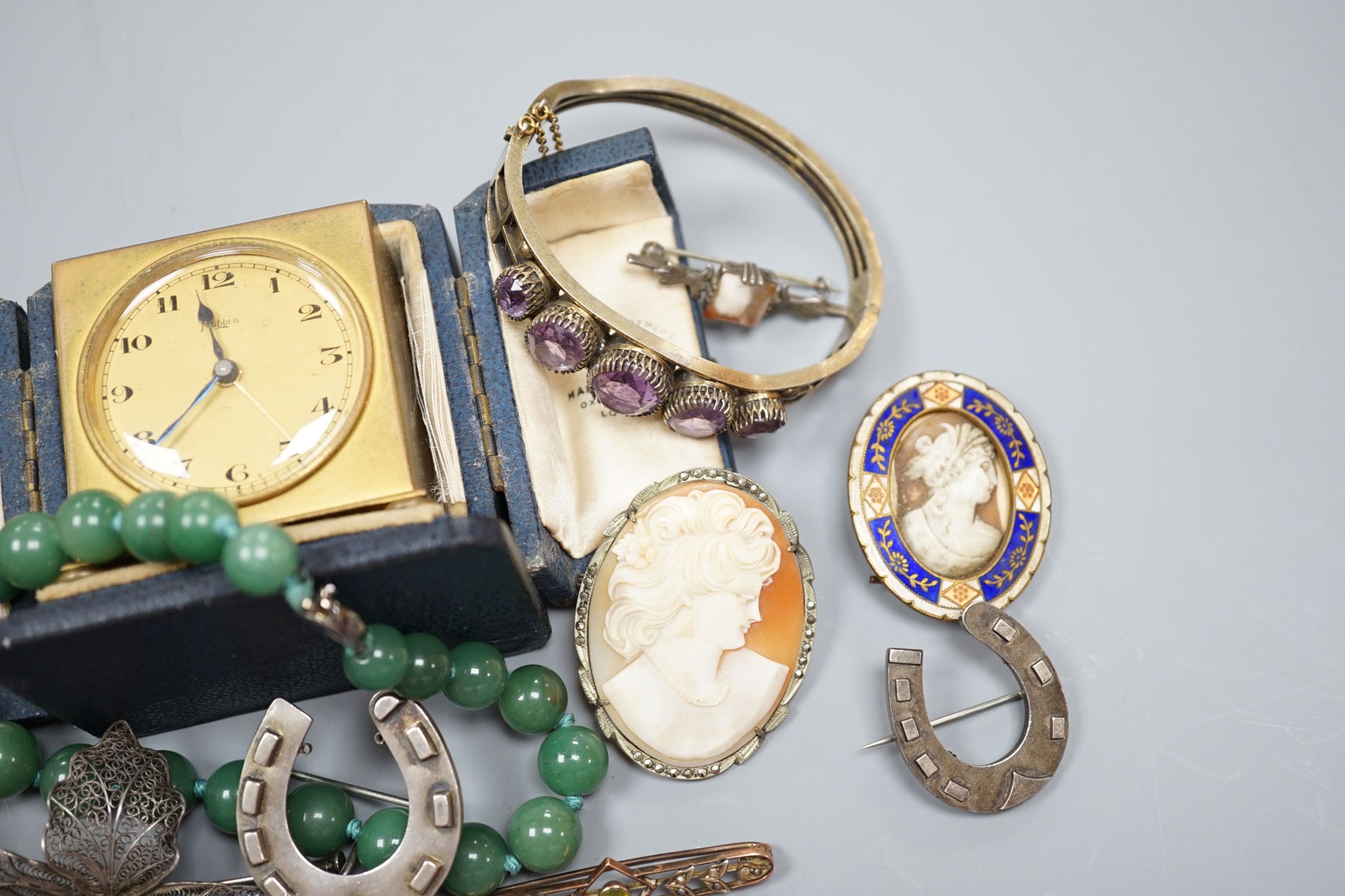 A small collection of jewellery including a silver horseshoe brooch, 9ct suspension brooch, gross 2.8 grams, and a travelling bedside timepiece and beaker.